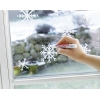 Eine Hand verwendet einen roten Kreidemarker, um weiße Schneeflocken auf ein Fenster zu zeichnen.