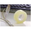 Klarer Rollenklebeband in gelber Farbe neben einem USB-Kabel auf einem Schreibtisch.