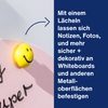 Magnet mit Smiley-Gesicht, auf einem Notizzettel an einer Oberfläche befestigt.
