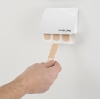 Hand, die ein Pflaster aus einem weißen Wandspender zieht, an einer hellen Wand montiert.