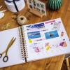 Auf einem Holztisch liegt ein offenes Scrapbook mit Bildern, Etiketten und Bastelmaterialien.