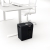 Schwarzer Aktenvernichter neben einem Tisch und Stuhl im Büro mit minimalistischem Design.