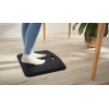 Ergonomische schwarze Anti-Ermüdungsmatte mit Füßen auf der Oberfläche, platziert an einem Tisch.