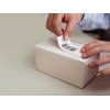 Eine Person klebt ein DYMO® Vielzwecketikett auf eine weiße, rechteckige Verpackung.