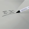 Graues Glasboard mit handschriftlicher "TO DO" Notiz und einem Marker in Nahaufnahme.