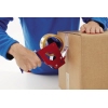 Person klebt transparentes Packband mit einem Abroller auf eine braune Versandbox.