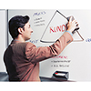 Mann schreibt mit einem Tafelschreiber auf ein Whiteboard, Tafelschreiberhalter im Vordergrund.