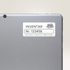 Folienetikett mit der Aufschrift "INVENTAR Nr. 123456" auf einem grauen Tablet.