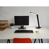 Schreibtisch mit schwarzer Tischleuchte, Monitor, Tastatur und Stifte auf einem weißen Tisch.
