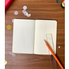 Offenes Notizheft auf einem Tisch mit Bleistift und Lineal, umgeben von bunten Bastelmaterialien.