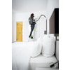 Person mit Rucksacksauger auf einer Leiter, die eine Wand in einem Schlafzimmer reinigt.
