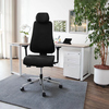Schwarzer Bürodrehstuhl mit Kopfstütze steht vor einem Schreibtisch in einem modernen Büro.