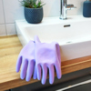 Lila Gummihandschuhe liegen auf einer Holzoberfläche neben einem Waschbecken.