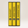 Drei gelbe Ordner mit beschrifteten Etiketten für "BUDGET", "MEETINGS" und "MARKETING".