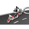 Schlüsselanhänger in Form eines Motorrads mit Helm, auf einer grauen Straßenoberfläche platziert.