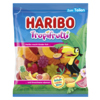 Tüte mit HARIBO Tropi Frutti Fruchtgummis in bunten Formen und Farben vor tropischem Hintergrund.