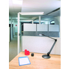 Stehleuchte mit großem Leuchtenkopf auf einem Tisch in einem Büro mit Trennwänden.