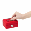 Rote Geldkassette mit Einwurfschlitz und Hand, die eine Münze hineinlegt.