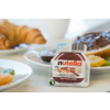 Ein Portionsbecher Nutella Nuss-Nugat-Creme auf einem Tisch mit Croissants und Obst.