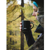 Schwarzer Thermobecher in Hand eines Benutzers, umgeben von einer herbstlichen Waldlandschaft.