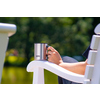 Edelstahl-Thermobecher in Hand einer Person auf einer weißen Gartenliege am Wasser.
