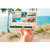 Hand hält goldenen Füllfederhalter über einer Postkarte mit Urlaubsfotos am Strand.