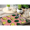 Tischset mit Avocado-Muster auf einem Holztisch mit Besteck und Gläsern.