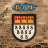 Wappen von Köln, auf einer Mauer angebracht, mit goldenen Kronen und schwarzen Heringen.