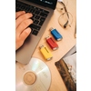 Drei Verbatim USB-Sticks in Gelb, Rot und Blau liegen neben einem Laptop auf einem Tisch.