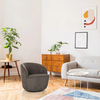 Runder Loungesessel in Grau vor einer modernen Wohnzimmereinrichtung mit Pflanzen und Kunst.