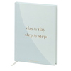 Hellblaues Notizbuch mit goldfarbener Prägung "day by day, step by step" auf dem Cover.