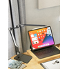 Schwarze Tischleuchte mit Gelenkarm und iPad auf einem Schreibtisch vor Vorhängen.