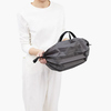 Faltbare Tragetasche in Charcoal, gehalten von einer Person in einem hellen Outfit.