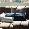 Zwei verschiedene Kissen mit Text und Mustern auf einer Couch in einem hellen Raum.