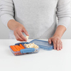 Person nimmt Lebensmittel aus einer offenen Sistema Lunchbox mit Fächern auf einem Tisch.