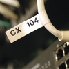Weißes Schriftband mit der Beschriftung "CX 104" auf einem Kabel in einem technischen Umfeld.