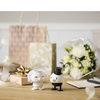 Dekorationsfigur eines Brautpaars in fröhlichen Farben vor Geschenken und Blumen.