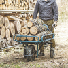 Eine Person schiebt eine Schubkarre mit Holzstämmen auf einem Waldweg.