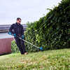 Mann nutzt einen Akku-Rasentrimmer neben einer hohen Hecke auf einem Rasen.