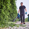 Mann führt einen Makita Laubsauger auf einem gepflasterten Weg entlang von Hecken.