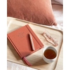 Rose gold Kugelschreiber auf einem Tablett neben einem Notizbuch, Brille und Tasse.