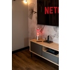 Pinkfarbene Lavalampe auf einem Sideboard mit Fernseher im Hintergrund.