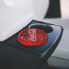 Lufterfrischer im Design eines Coca-Cola-Flaschenverschlusses auf einem Fahrzeuginnenraum.