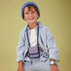 Ein Kind trägt einen blauen Brustbeutel in einem modischen Outfit vor einem neutralen Hintergrund.