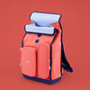 Schulrucksack in bunten Farben mit zwei Taschen und Rolltop-Verschluss auf rotem Hintergrund.