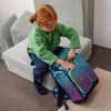Schulranzen in türkis-violett mit neonfarbenen Akzenten, neben einem Kind auf einem Sofa.