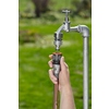 Hochwertiger Schlauchverbinder in Hand, angeschlossen an einen Wasserhahn im Freien.