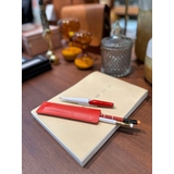 Rotes Schreibgeräteetui mit Stiften auf einem Notizblock auf einem Tisch.