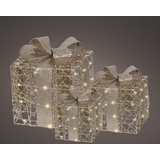 Drei dekorative Geschenkschachteln mit Lichtern und Schleifen in Goldfarbe auf dunklem Hintergrund.