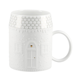 Weiße Tasse in Hausform mit Prägung, dekorativen Dachziegeln und goldenem Türdetails.